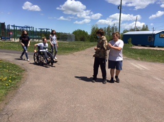 Group of five students on a cement path, two are in front and three are behind. One student is using a wheelchair